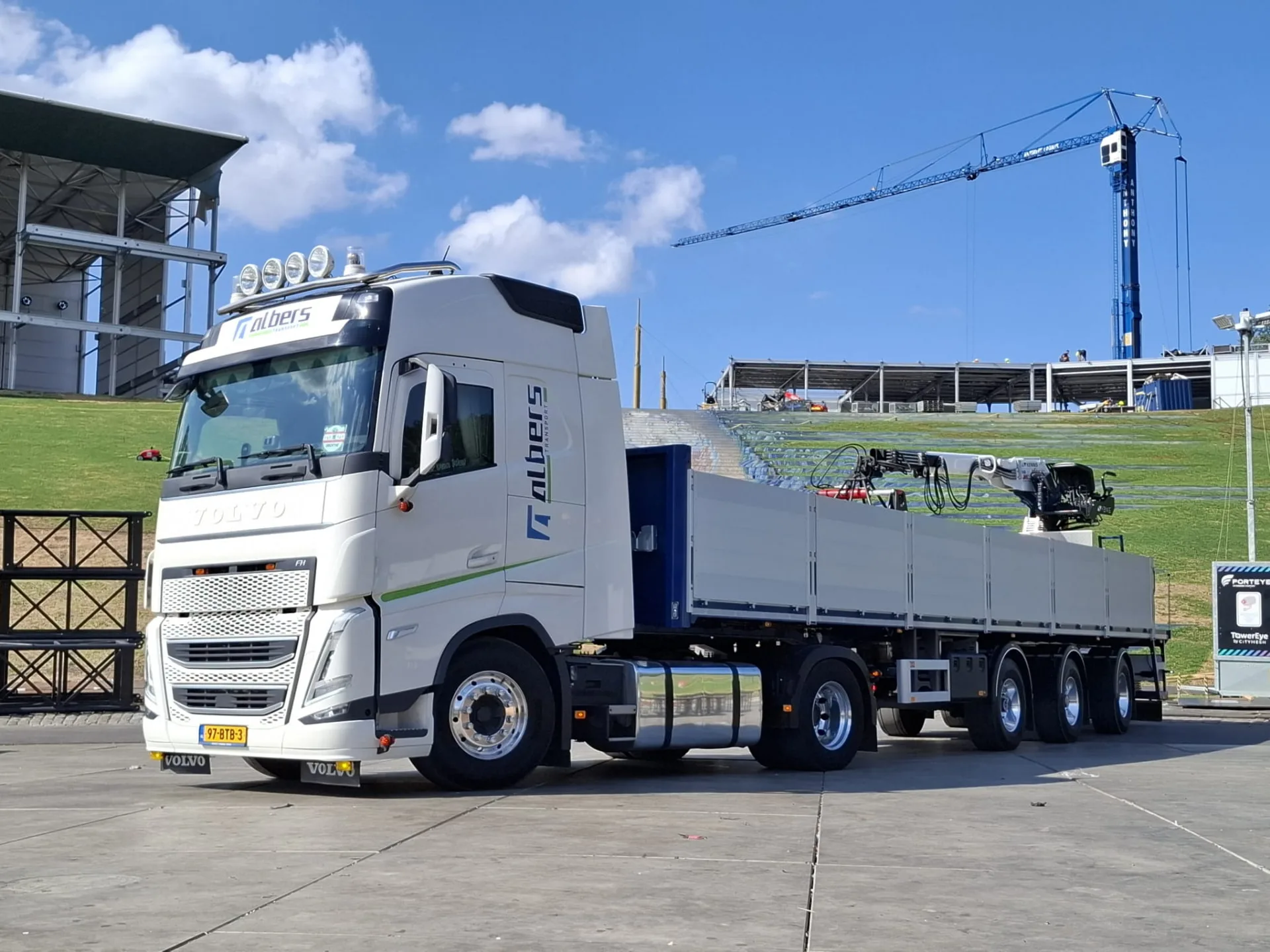 Albers-vrachtwagen met autolaadkraan en open oplegger op een bouwlocatie