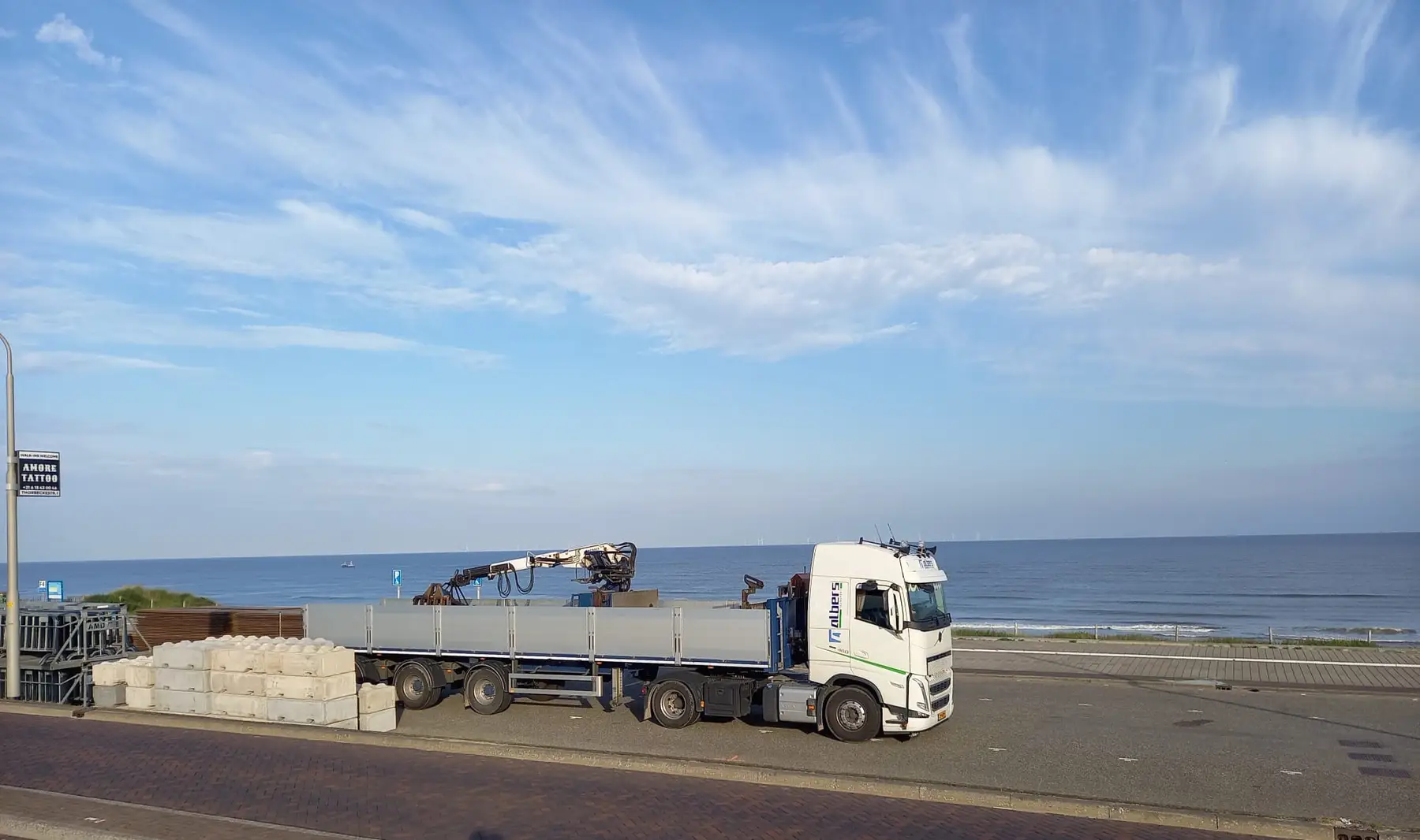 Albers-vrachtwagen met betonblokken aan de boulevard bij de zee