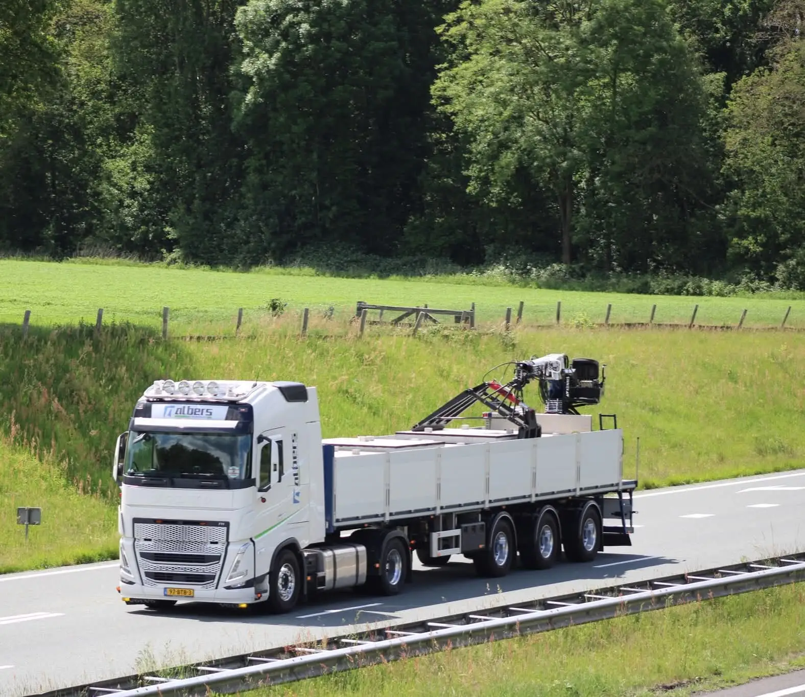 Albers-vrachtwagen met autolaadkraan op de snelweg langs een weiland