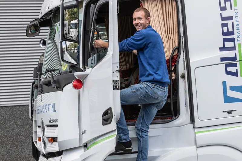 Lachende chauffeur stapt in zijn Albers-vrachtwagen
