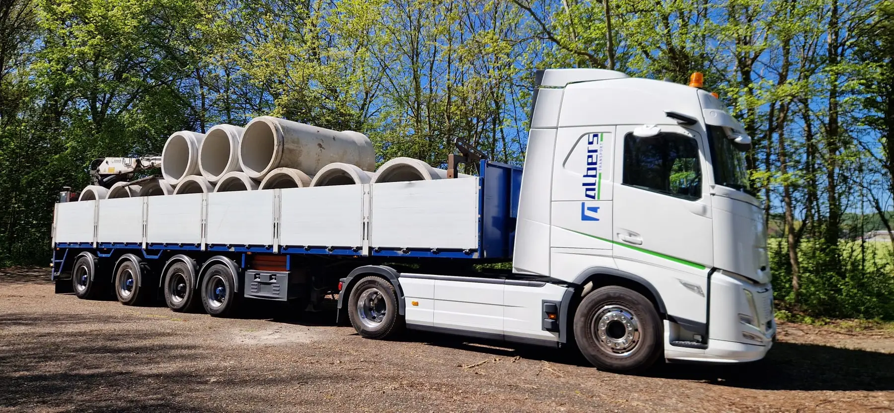 Albers-vrachtwagen geladen met betonnen buizen langs de bosrand